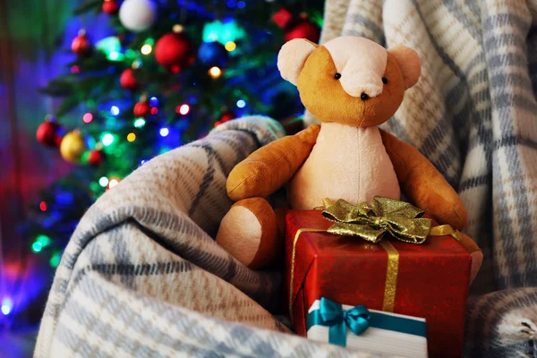 Osito de peluche y caja de regalo en mecedora sobre fondo de árbol de Navidad — Foto de Stock