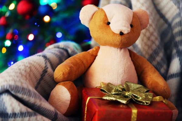 Medvídek a krabičky v houpacím křesle na pozadí vánoční stromeček — Stock fotografie