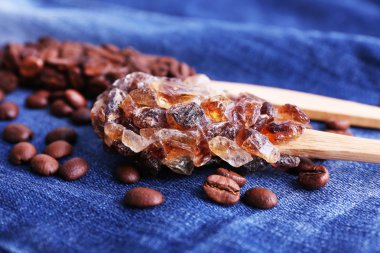 Sticky wooden spoons with coffee beans and crystals of on jeans background clipart