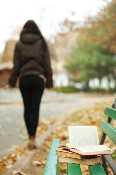 Boken lämnade på bänken med silhuetten av flicka gå bort i höst park — Stockfoto