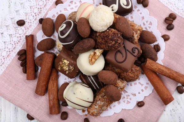 Heap of sweet chocolates with coffee beans on pink material and white doily on wooden background — Stock Photo, Image