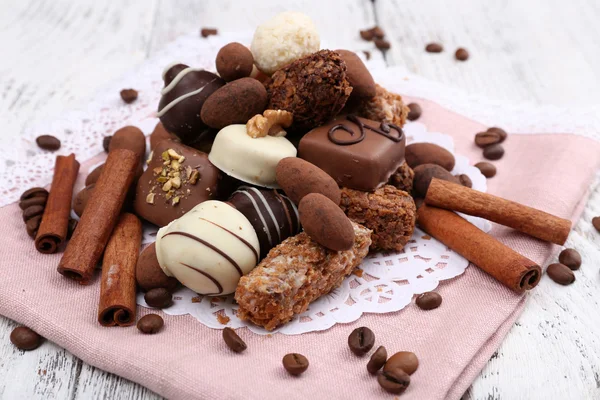 Montón de chocolates dulces con granos de café sobre material rosa y tapete blanco sobre fondo de madera —  Fotos de Stock