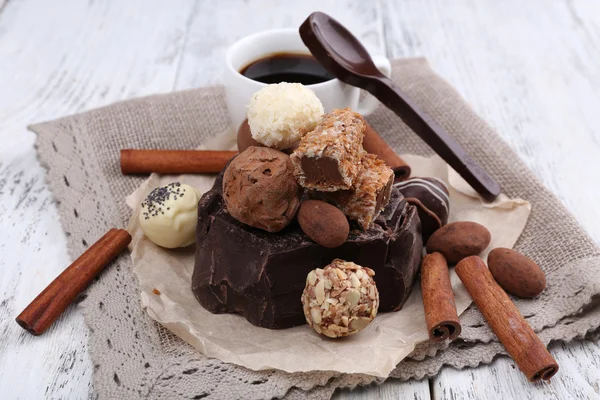 Hög med bit av choklad och tryffel med kanelstång på söndersmulad papper, grå material och trä bakgrund — Stockfoto
