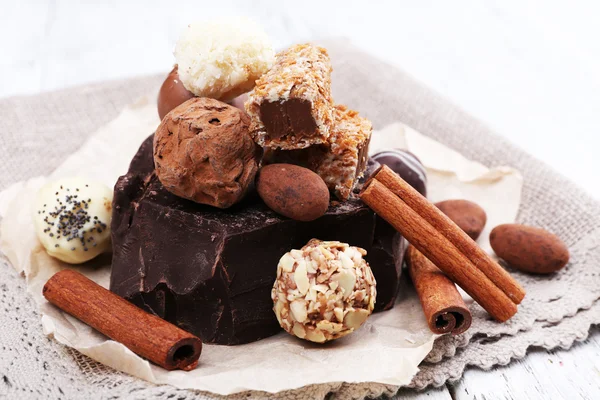 Pile de morceaux de chocolat et de truffes avec bâton de cannelle sur papier émietté, matière grise et fond en bois — Photo