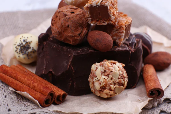 Pile of chunk of chocolate and truffles with cinnamon stick on crumbled paper, grey material and wooden background — Stock Photo, Image