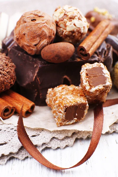 Pile of chunk of chocolate and truffles with cinnamon stick on crumbled paper, grey material and wooden background — Stock Photo, Image