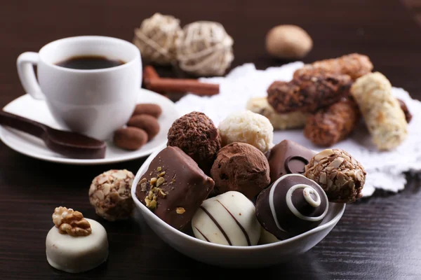 Une tasse de café et une soucoupe avec des chocolats sur napperon, sur le fond lisse en bois foncé — Photo