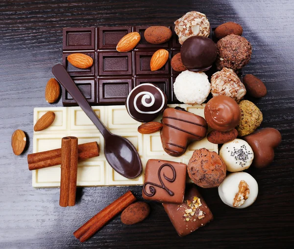 Бары белого и горького шоколада с конфетками и сладкой ложкой на темном гладком деревянном фоне — стоковое фото