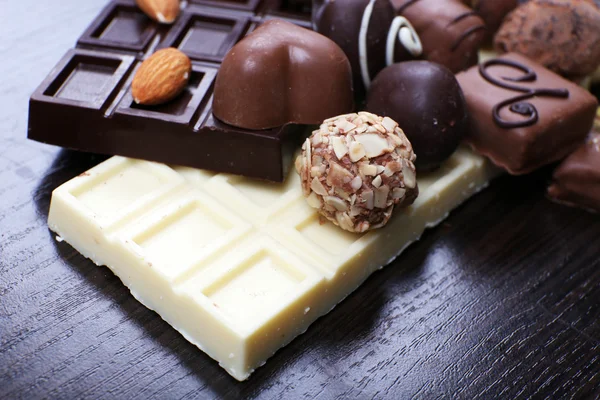 Barras de chocolates blancos y amargos con caramelos, bastón de canela y almendras sobre el fondo liso de madera oscura —  Fotos de Stock