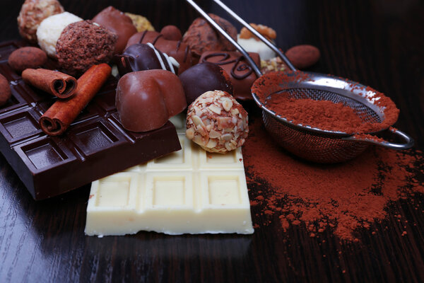 Bars of chocolate, sweet candies and strainer with cocoa on the dark wooden smooth background