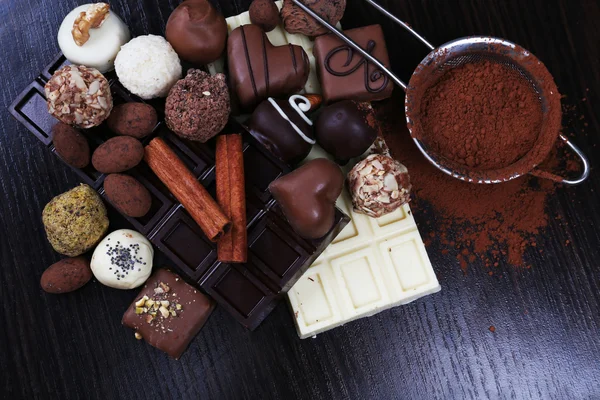 Bares de chocolate, doces e coador com cacau no fundo liso de madeira escura — Fotografia de Stock