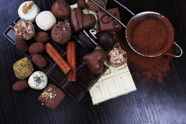 Bars of chocolate, sweet candies and strainer with cocoa on the dark wooden smooth background