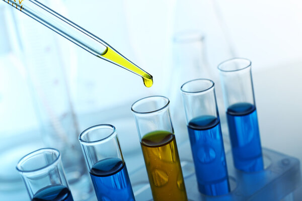 Pipette adding yellow fluid to one of several test-tubes with flasks on light background