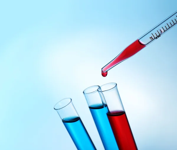 Pipette che aggiunge fluido rosso a quello delle provette su fondo chiaro — Foto Stock