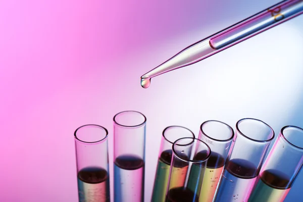 Pipette adding liquid to the one of test-tubes on the pink shining background — Stock Photo, Image