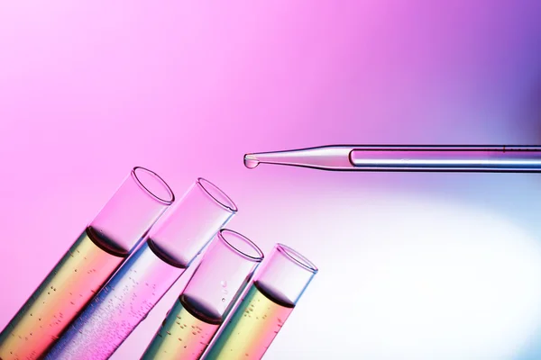 Pipetteer vloeistof toe te voegen aan één van test-buizen op de roze achtergrond schijnt — Stockfoto