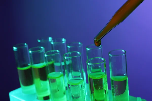 Pipette adding liquid to the one of test-tubes on dark background — Stock Photo, Image