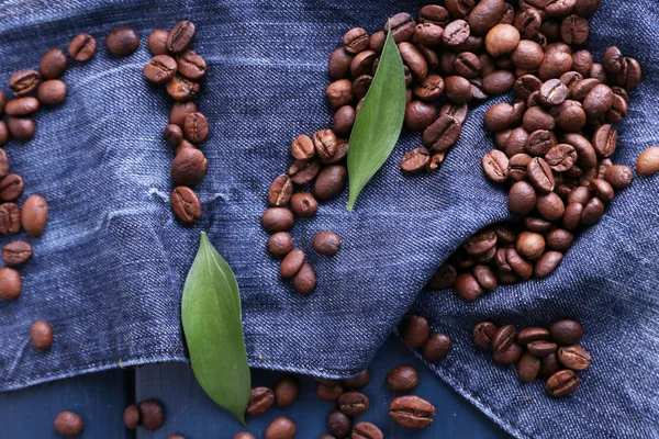 Grünes Blütenblatt mit Kaffeebohnen auf blauem Holzhintergrund mit Jeansmaterial — Stockfoto