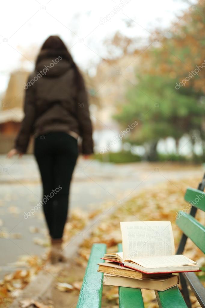 Book left on the bench with silhouette of girl walking away in autumn park