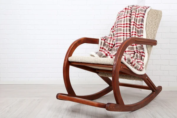 Confortevole sedia a dondolo con tappeto sul pavimento in legno vicino allo sfondo muro di mattoni — Foto Stock