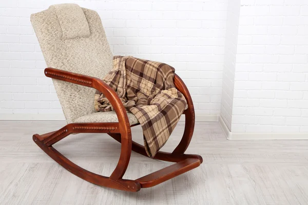 Кресло-качалка, покрытое клеткой на деревянном полу рядом с кирпичной стеной — стоковое фото