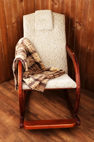 Крісло-качалка вкрита плед на дерев'яному фоні стіни — стокове фото