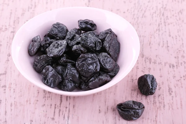 Bowl of prunes on color wooden background — Stock Photo, Image