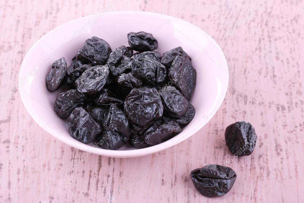 Bowl of prunes on color wooden background
