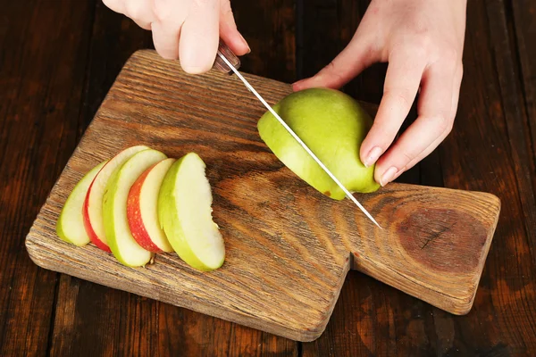 Mains de femmes coupant des pommes à bord sur fond de table en bois — Photo