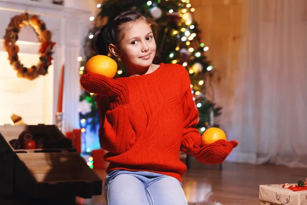 Menina bonito com laranja perto da árvore de Natal — Fotografia de Stock