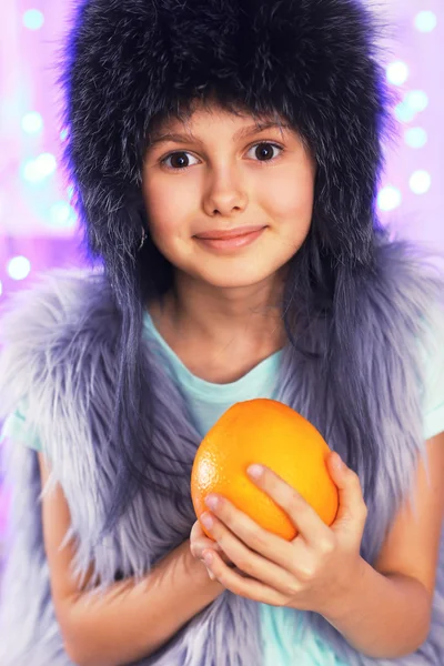 Roztomilá holčička s pomerančem na pozadí světla — Stock fotografie