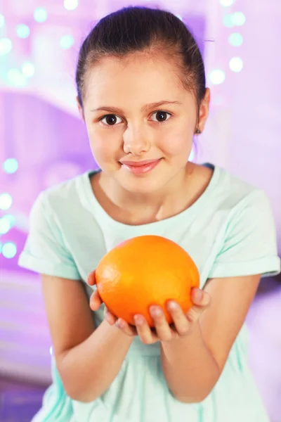 Cute little girl with orange on lights background — Stock Photo, Image