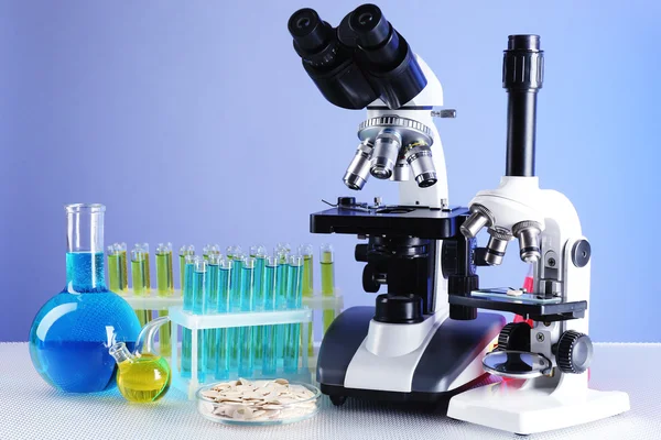 Microscopen, petrischaal met monsters van graan en reageerbuizen op tafel, op kleur achtergrond — Stockfoto