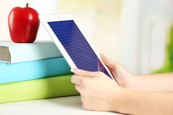 Mão feminina segurando tablet PC perto de livros, close-up. Conceito de educação moderna — Fotografia de Stock