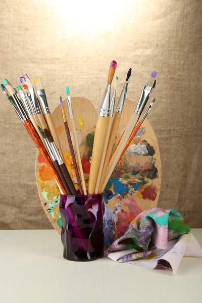 Paint brushes with paints and palette on beige background — Stock Photo, Image