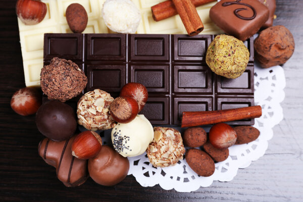 Bars of white and bitter chocolates with candies, hazelnut and cinnamon stick on the dark wooden smooth background with doily