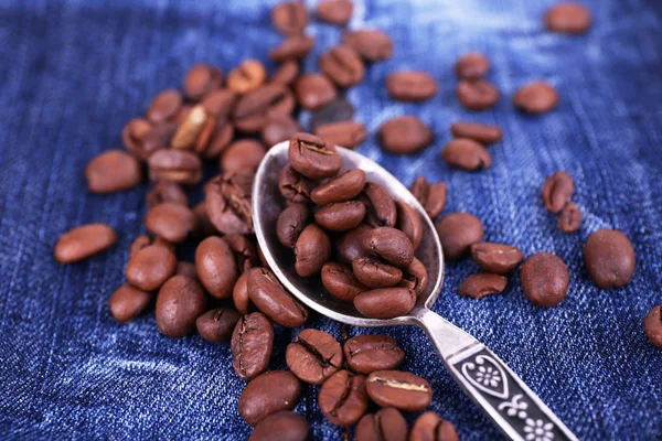 Spoon with coffee beans on ripped jeans background — Stock Photo, Image