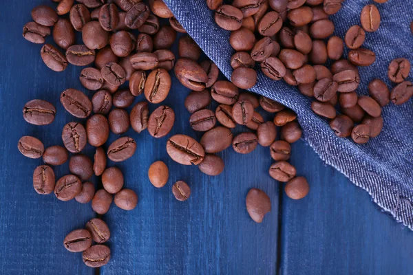 Verschüttete Kaffeebohnen auf blauem Holzhintergrund mit Jeansmaterial — Stockfoto