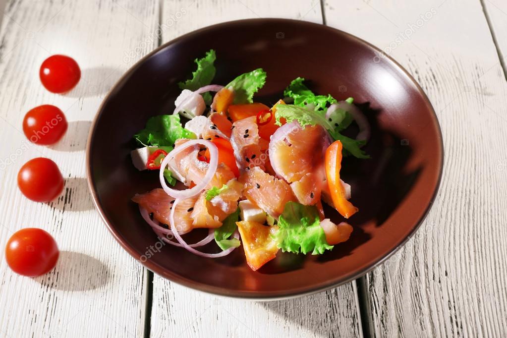 Fresh fish salad with vegetables on plate on wooden table close-up