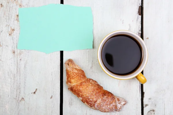 Composizione di caffè, croissant fresco e cartoncino su fondo legno — Foto Stock