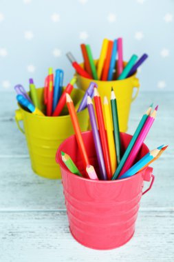 Üç plastik bardakla farklı kalem, kalem ve işaretleri renk ahşap masa ve yazdırılan yıldız ile mavi arka plan rengi ahşap tablo