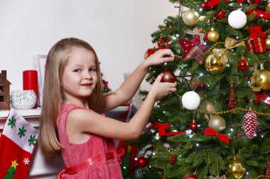 Parlak arka planda Noel ağacı süsleyen küçük kız.