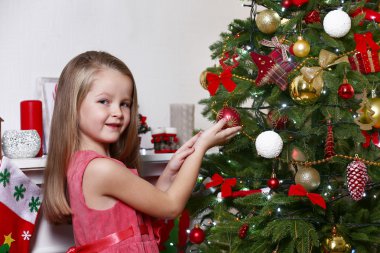 Parlak arka planda Noel ağacı süsleyen küçük kız.