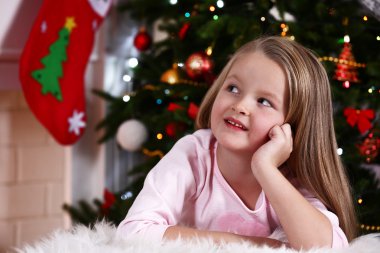 Little girl lying on fur carpet on Christmas tree background
