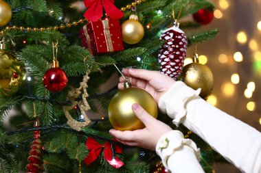 Child's hands hanging bauble on Christmas tree on bright background