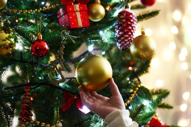 Child's hands hanging bauble on Christmas tree on bright background