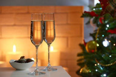 Two glass with champagne with bowl of chocolates on table on Christmas tree and fireplace with candles background