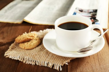 Cup of coffee with cookies on burlap cloth near newspaper on wooden table background