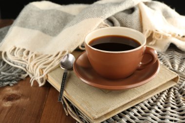Cup of coffee on book near plaid on wooden table background