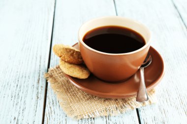 Cup of coffee with cookies and spoon on burlap cloth, on color wooden background